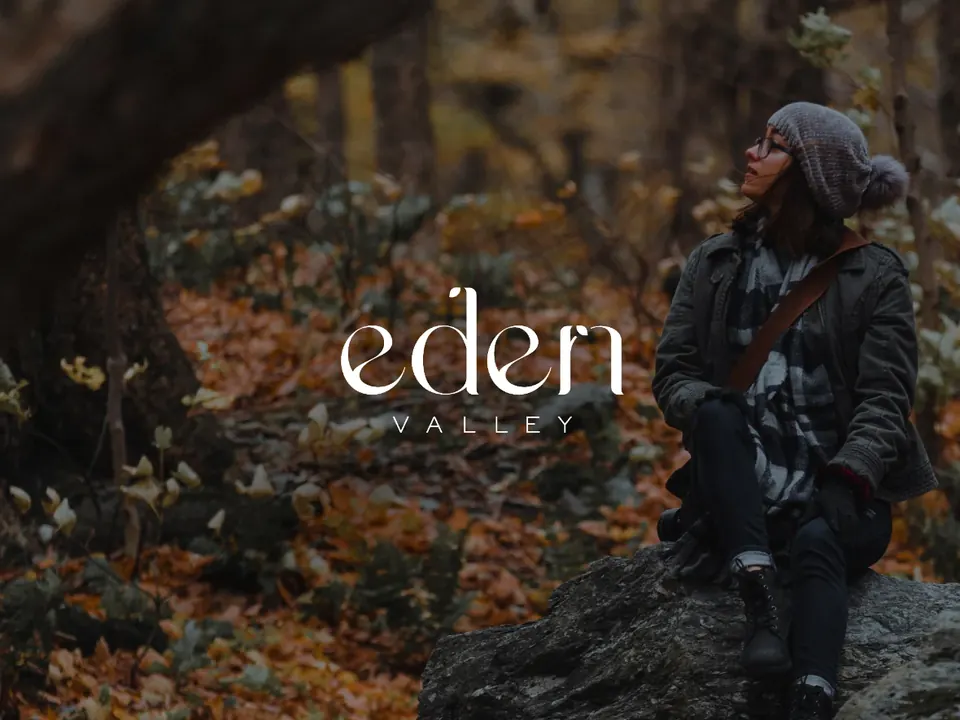 A person sits on a rock in an autumn forest beside the Eden Valley logo.